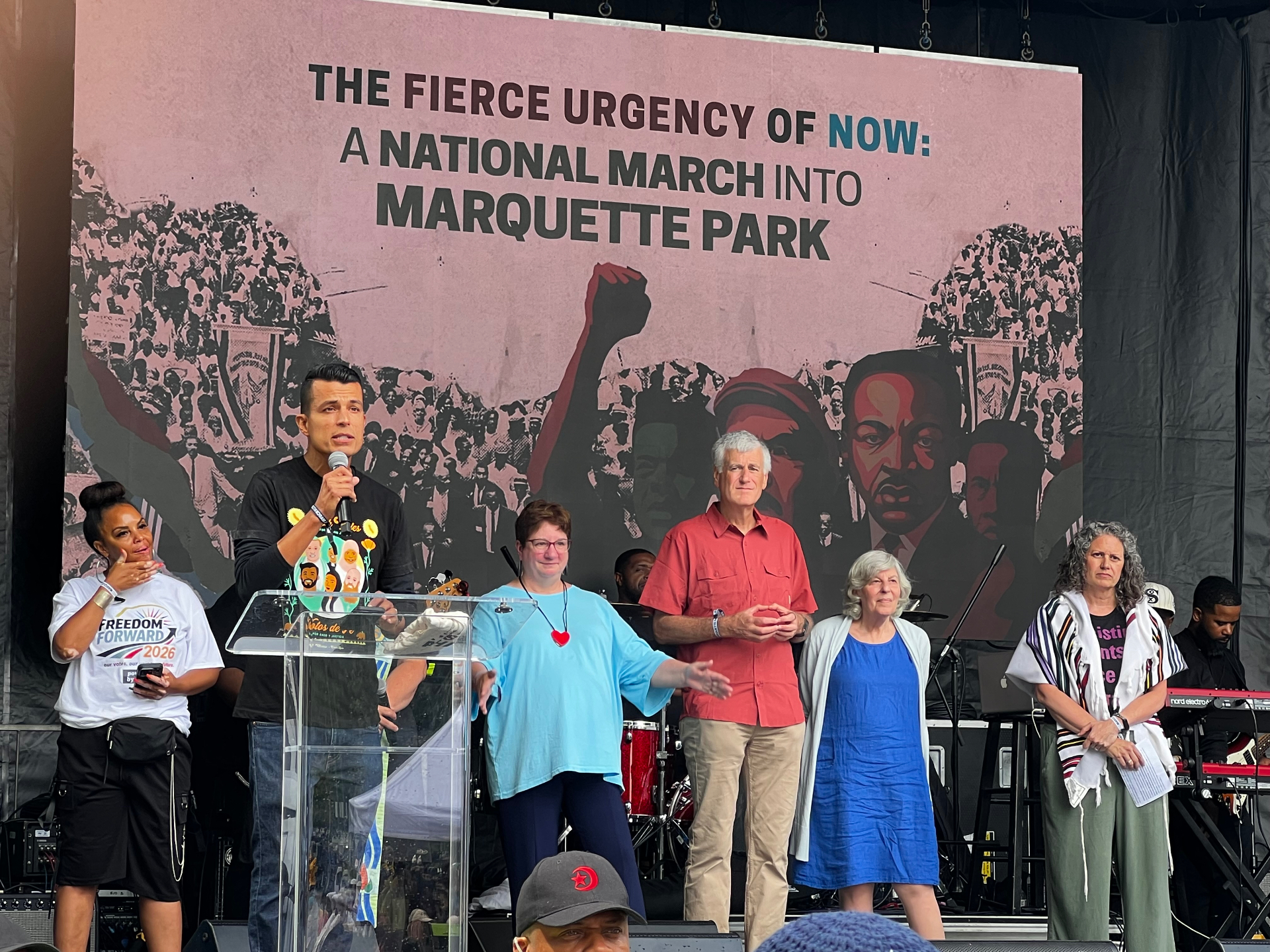 Interfaith leaders standing together on stage as a speaker addresses the march