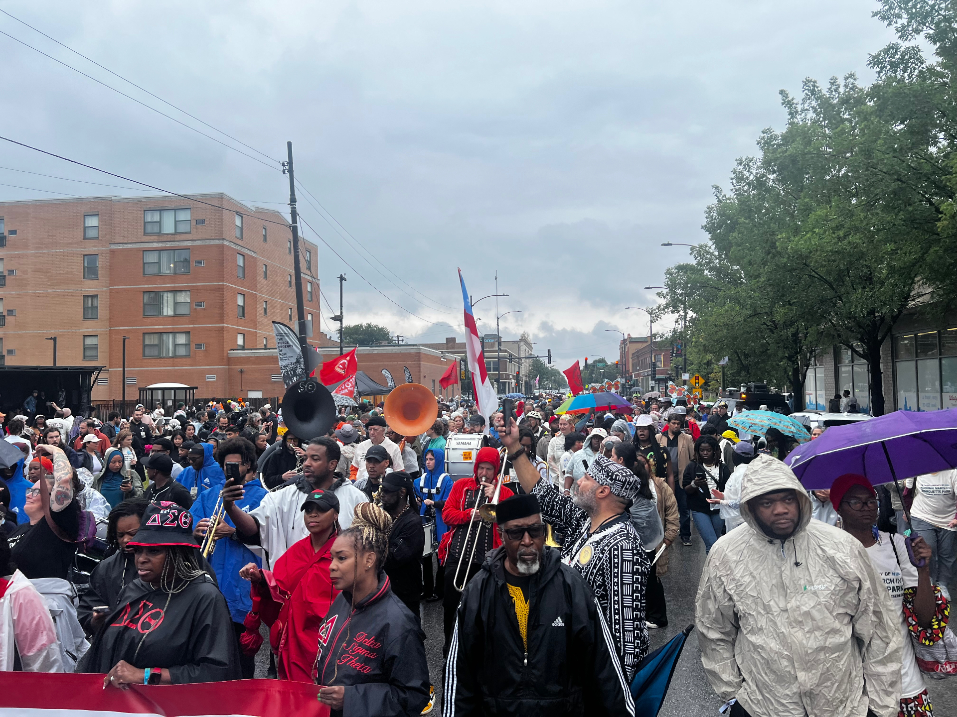 Thousands of marchers filling a Chicago street in the rain with flags, drums and umbrellas